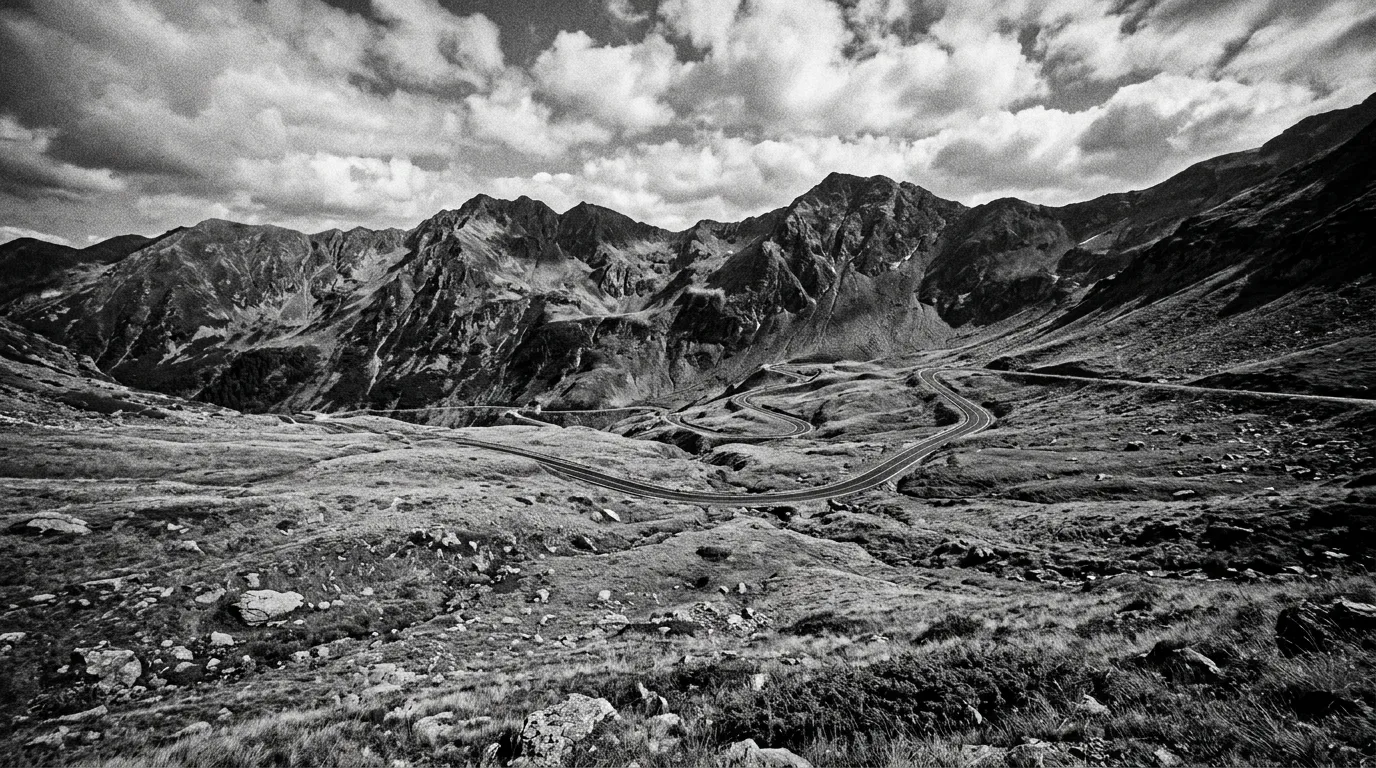 Droga Transfogarska przechodząca przez łąki alpejskie powyżej granicy lasu, serpentyny w oddali, szczyty Fogarasza